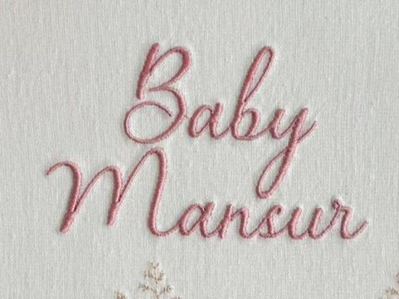 A inscri��o Baby Mansur bordada em cursiva rosa em duas linhas