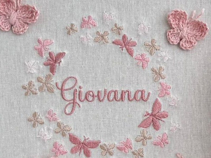 Coroa circular formada s� de borboletas bordadas em rosa, bege e branco, com o nome Giovana em cursiva ao centro