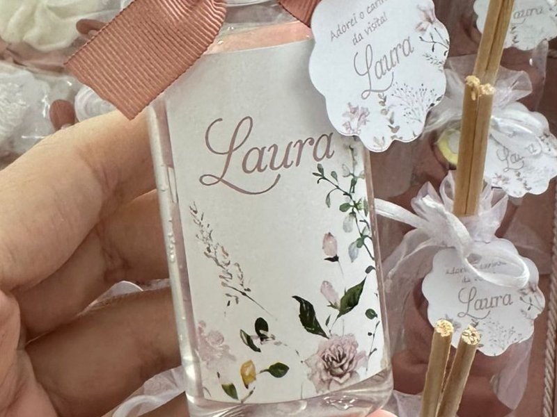 R�tulo do frasco de 60ml com flores delicadas e o nome Laura em cursiva, envolvendo o frasco transparente