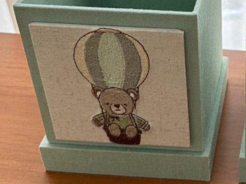 Placa de linho aplicada no cachep� com um urso bordado pendurado no cesto de um bal�o de ar quente listrado