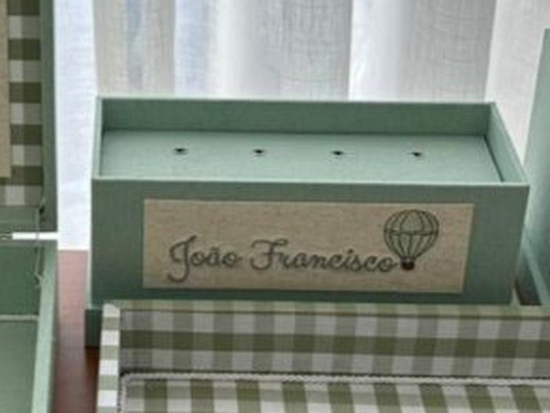 O cachep� quadrado verde com um bal�o e um ursinho bordados na face frontal