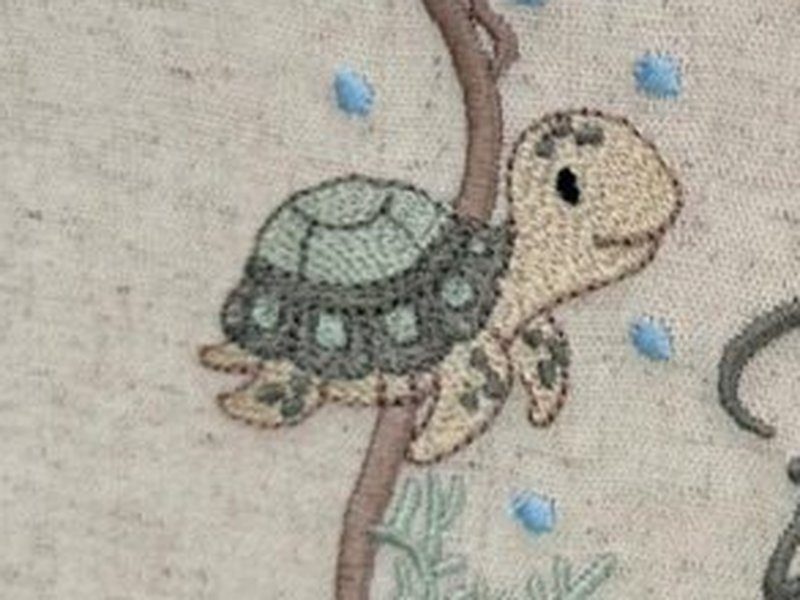 A tartaruga bordada � esquerda, com o casco em tons de verde e cinza e bolhas em volta