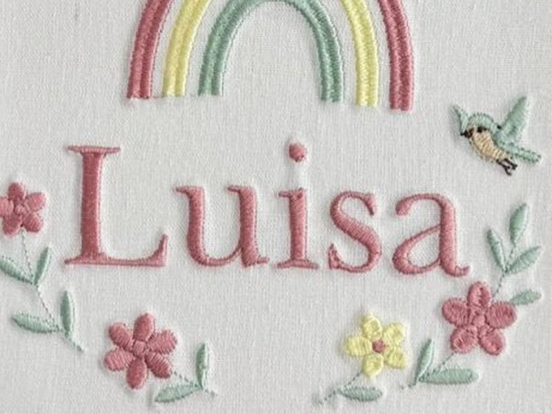 O nome Luisa bordado por inteiro em letra serifada rosa, com um passarinho verde-�gua � direita