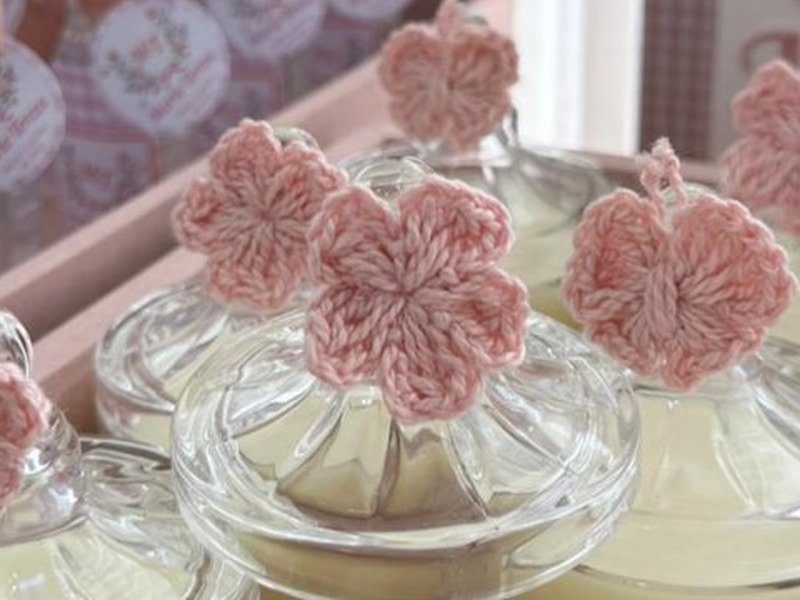 As flores de croch� em fio rosa amarradas com linha aos pegadores das tampas de vidro facetado