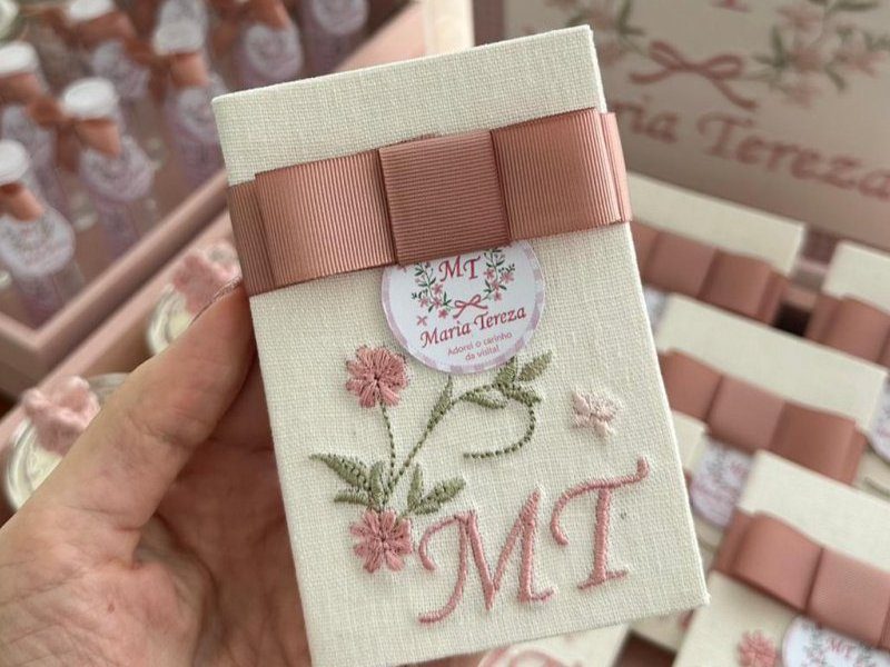 Capa de linho cru com 'MT' bordado em rosa e um ramo de flores, faixa de gorgur�o rosa-velho com la�o e tag redonda