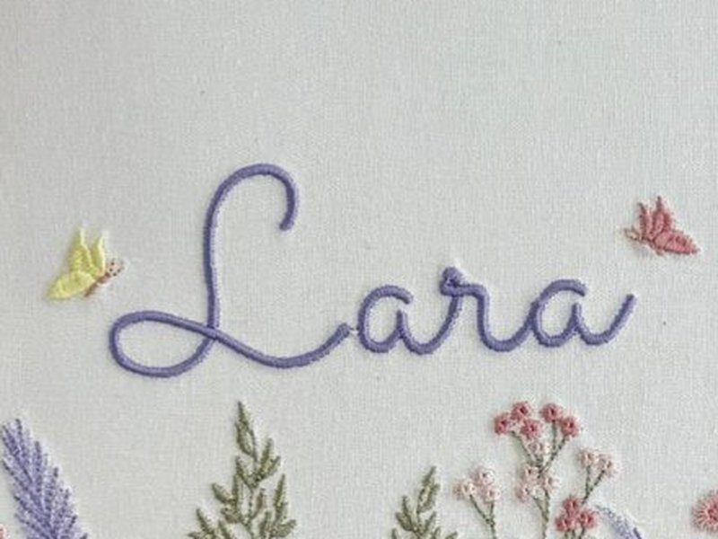 O nome Lara bordado por inteiro em cursiva roxa, com uma borboleta amarela � esquerda e uma rosa � direita
