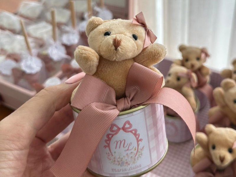 Um ursinho de pel�cia bege com la�o rosa na orelha, sentado dentro da lata dourada, com fita larga rosa amarrada em volta