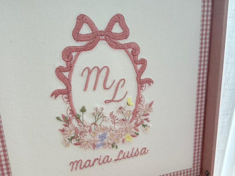 A fita rosa formando a cartela oval com la�o no topo, 'ML' em cursiva, flores e 'Maria Lu�sa' bordado abaixo