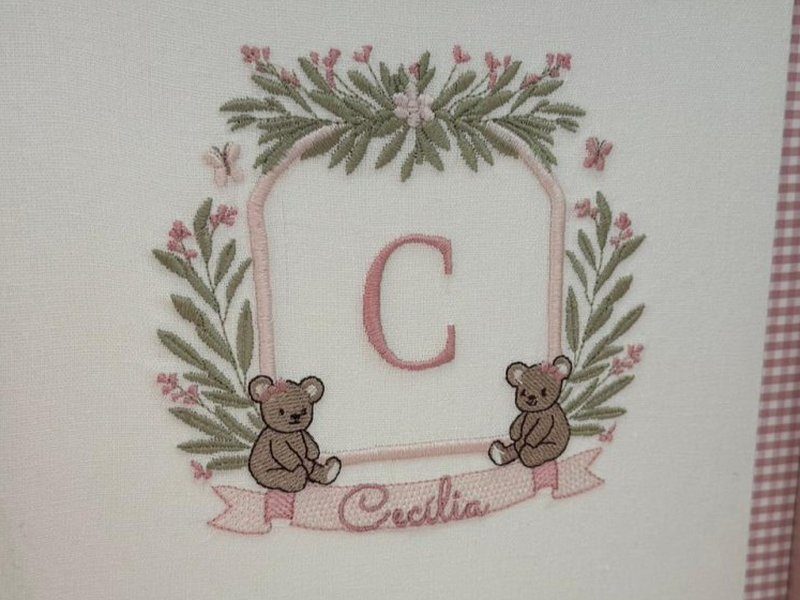 Cartela em arco de contorno rosa com a letra C, coroa de folhas verdes e flores rosa, e dois ursinhos sentados apoiados na faixa com 'Cec�lia'