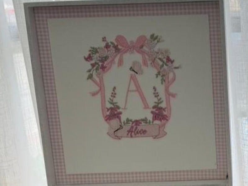 A faixa rosa com 'Alice' bordado, abaixo do buqu� de flores e da letra A