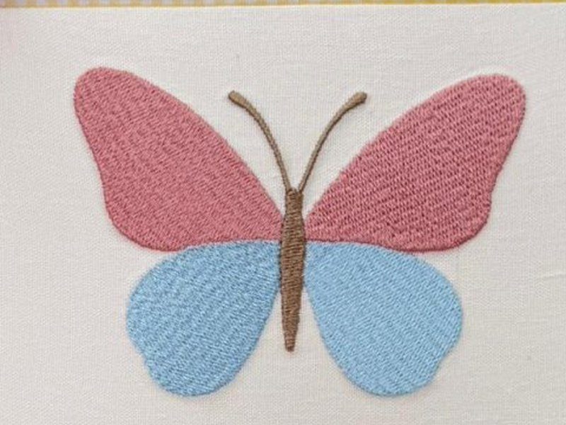 Borboleta grande com asas superiores rosa e inferiores azuis, corpo e antenas marrons, toda em ponto cheio