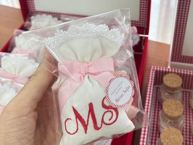 Sach� de tecido branco com barra de renda na boca, la�o rosa e MS bordado em vermelho, dentro do saquinho transparente