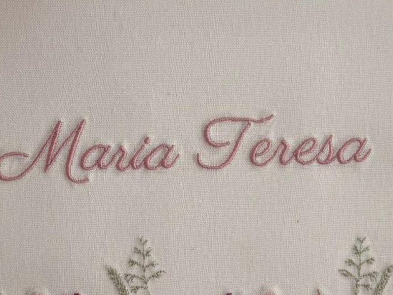 O nome Maria Teresa bordado por inteiro em cursiva rosa, numa linha s�