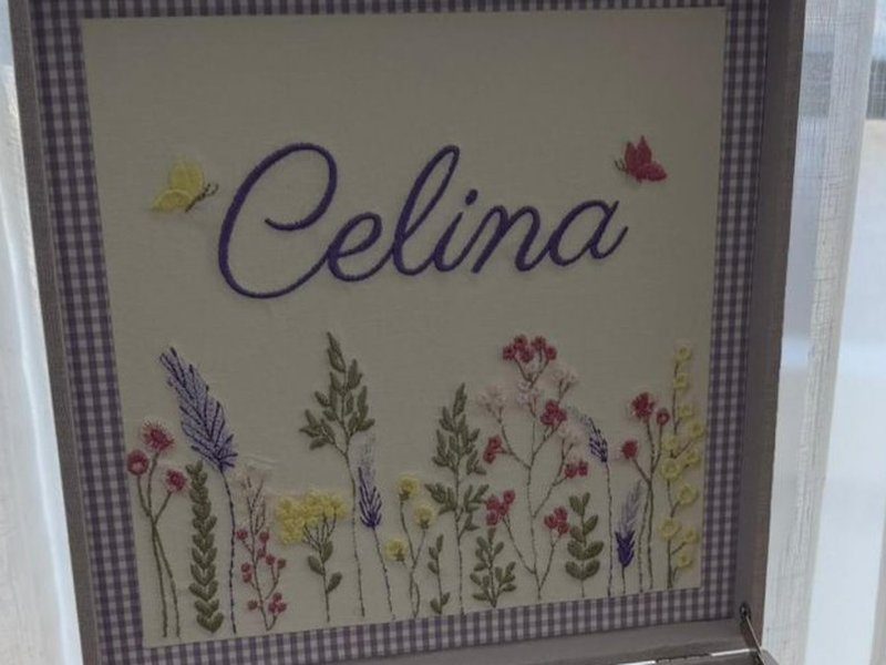 Painel interno da tampa com Celina em cursiva roxa e o campo de flores bordado, emoldurado em xadrez lil�s