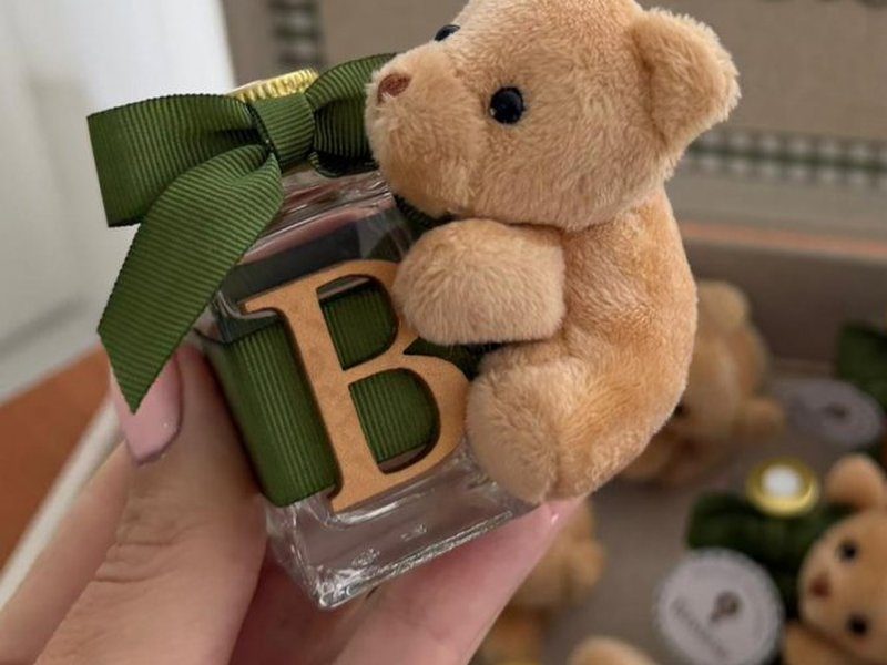 Frasco de vidro quadrado com tampa dourada e inicial B em madeira, com um ursinho de pel�cia abra�ado a ele e la�o verde escuro
