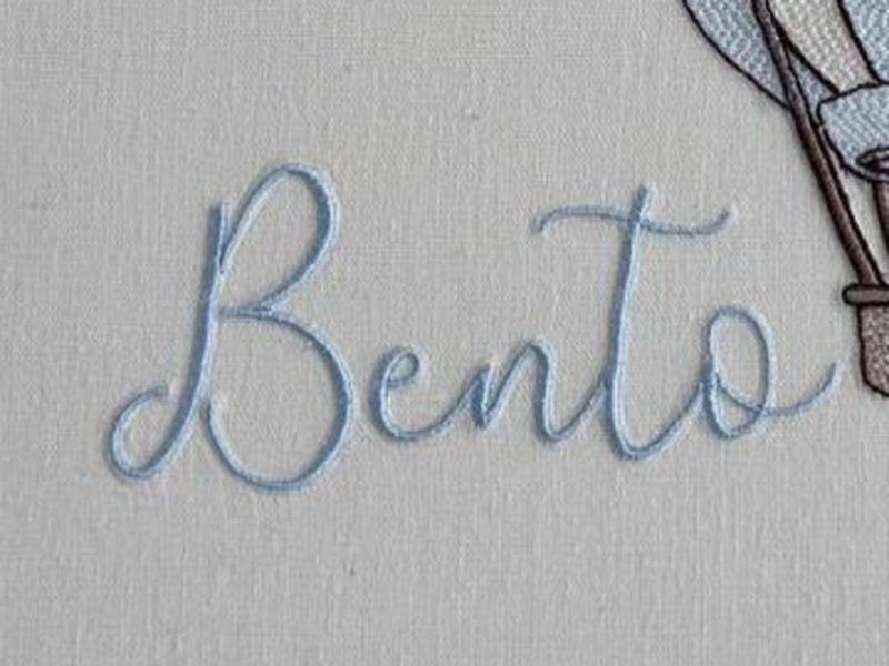 O nome Bento bordado por inteiro em cursiva azul, � esquerda e abaixo do bal�o, fora do eixo central