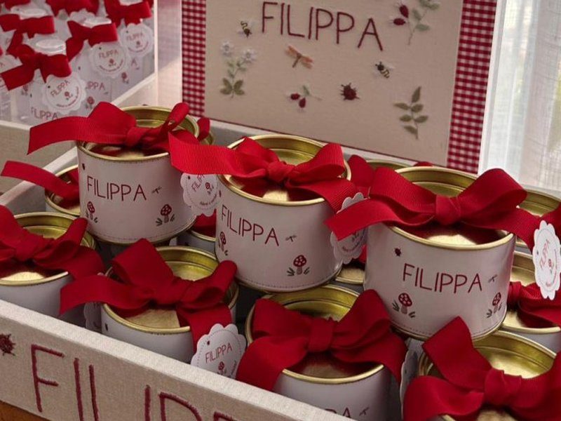 Latas de tampa dourada com r�tulo FILIPPA e la�o vermelho largo, alinhadas na bandeja