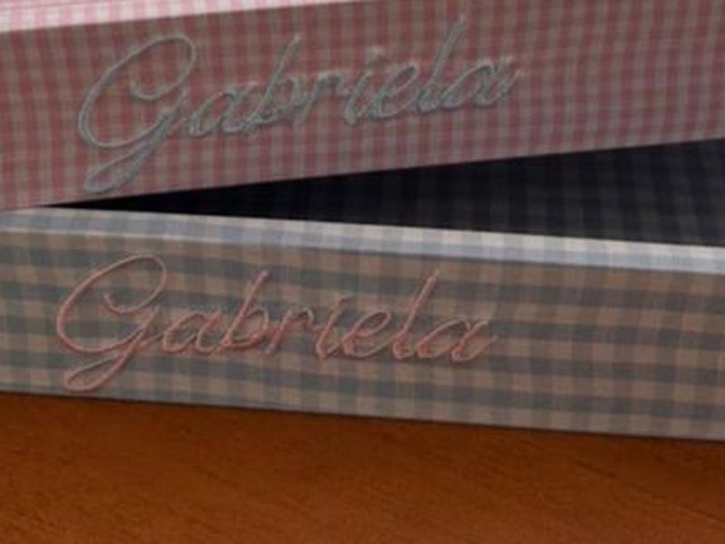 O mesmo nome Gabriela bordado em rosa na bandeja xadrez azul-acinzentado, invertendo as cores da outra pe�a