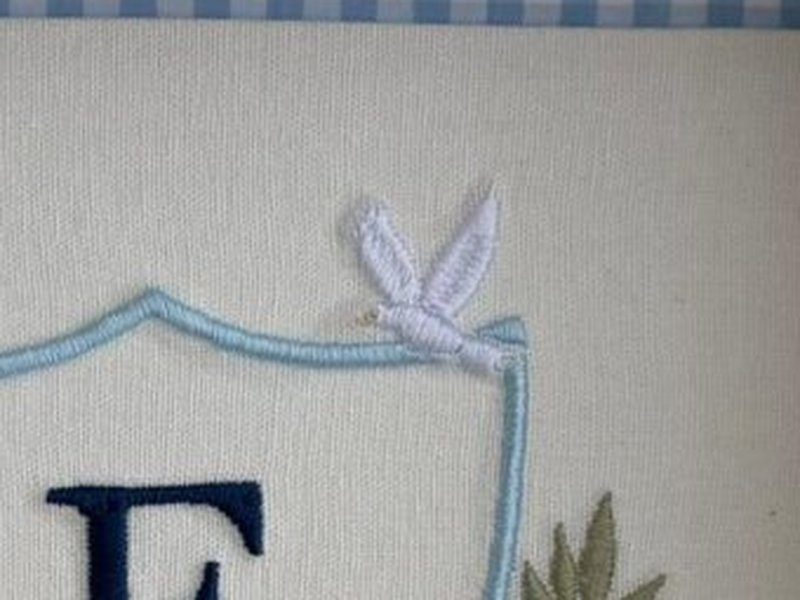 Pombinha branca bordada pousada no canto superior direito da borda do escudo, com as asas recolhidas