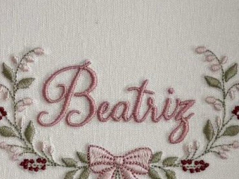 O nome Beatriz bordado por inteiro em cursiva rosa, dentro da coroa aberta