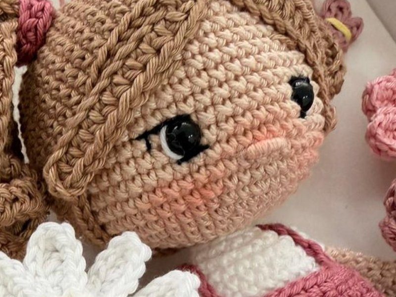 O rosto da boneca em macro: olhos bordados com ponto de luz branco, bochechas rosadas e as carreiras de ponto baixo do croch�