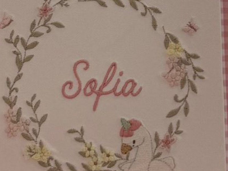 O nome Sofia bordado em cursiva rosa no centro da guirlanda de folhas e flores