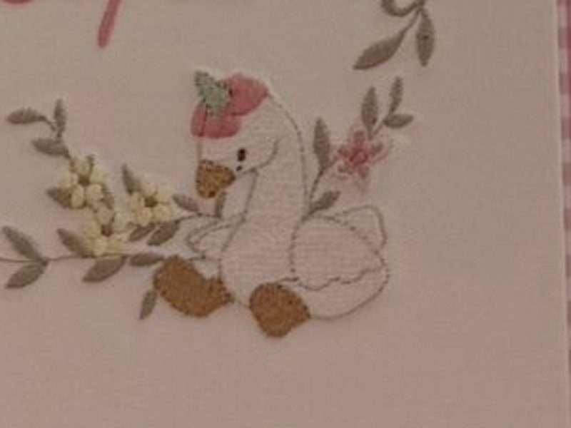 O ganso branco bordado com touca rosa e patas alaranjadas, na base da guirlanda