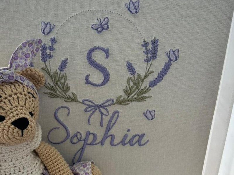 A letra S entre dois ramos de lavanda bordados em roxo e verde escuro, com borboletas e tulipas soltas, la�o e o nome Sophia em cursiva abaixo