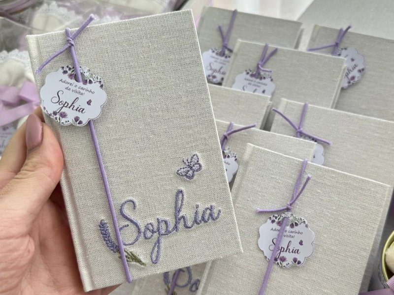 Moleskine revestido de linho com o nome Sophia bordado em lil�s, ramo de lavanda e borboleta bordados, el�stico lil�s e tag rendada