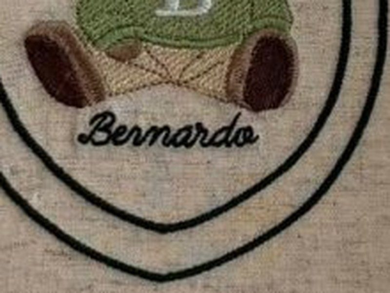O nome Bernardo bordado em cursiva escura dentro do escudo, sob o urso
