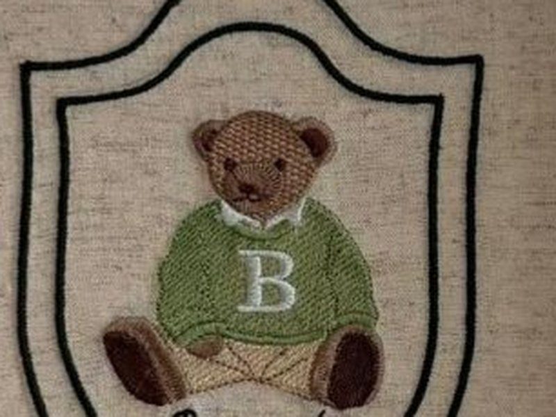 O urso bordado de su�ter verde com a inicial B no peito e colarinho branco