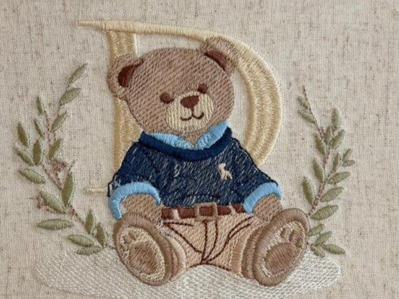 O urso de su�ter azul escuro sentado diante da letra D bege, entre dois ramos de folhas