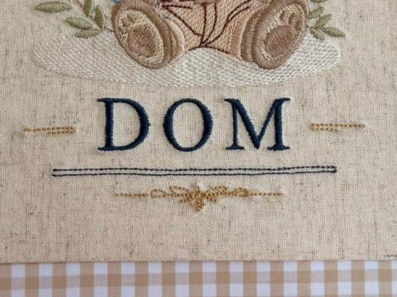 O nome DOM em letras serifadas azul escuro sobre um filete azul e um arabesco em fio dourado