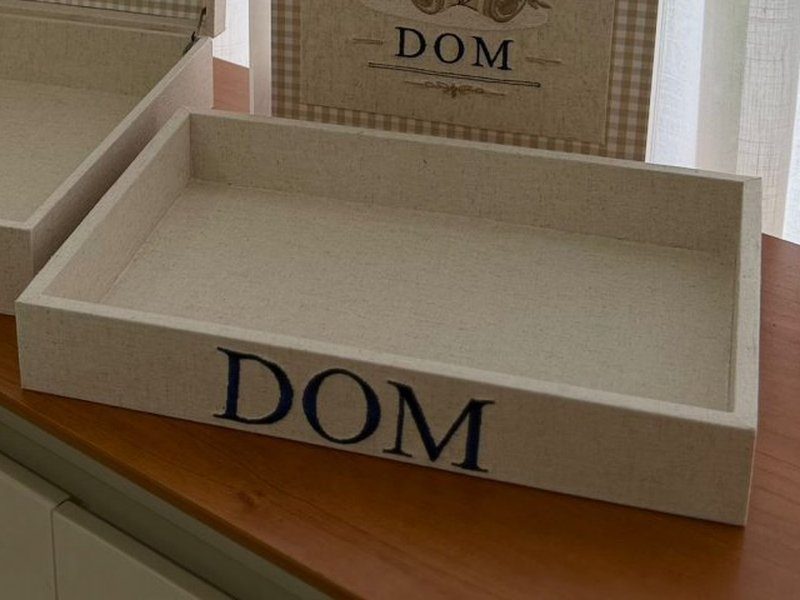 O nome DOM em letras azul escuro aplicadas na borda frontal da bandeja de linho cru