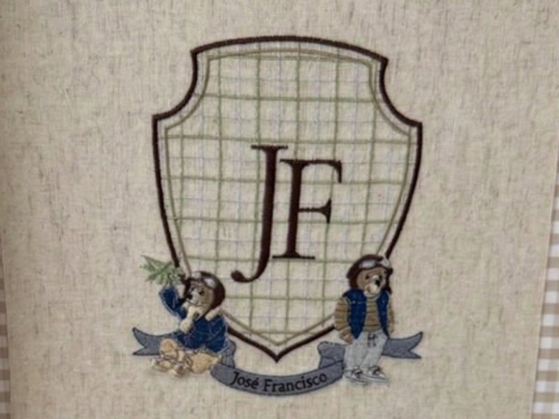 Escudo quadriculado bordado com JF ao centro, dois ursos de roupa azul nas laterais e faixa com o nome Jos� Francisco