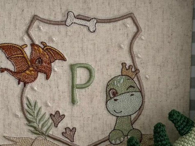 O escudo bordado com osso no topo, a letra P ao centro, o pterod�ctilo laranja e o dinossauro de coroa