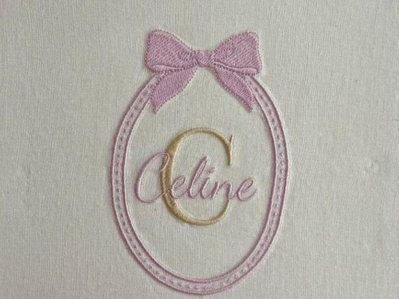 O oval pespontado com la�o rosa no topo, a letra C dourada e o nome Celine sobreposto em cursiva