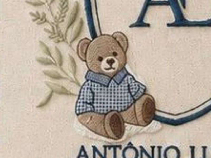 O urso bordado de camisa xadrez azul sentado na base do escudo, entre os ramos de folhas