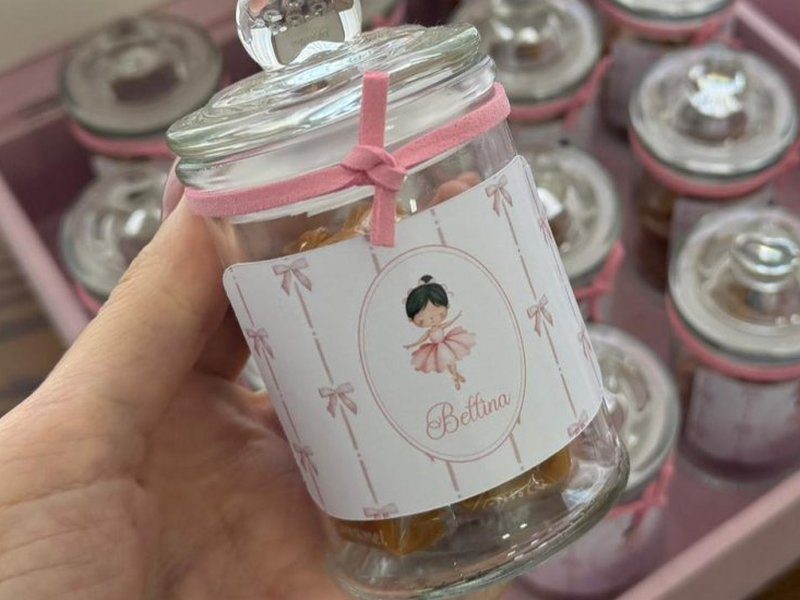 Baleiro de vidro com la�o de fita rosa no gargalo, r�tulo com a bailarina e o nome Bettina, e as balas caramelo vis�veis