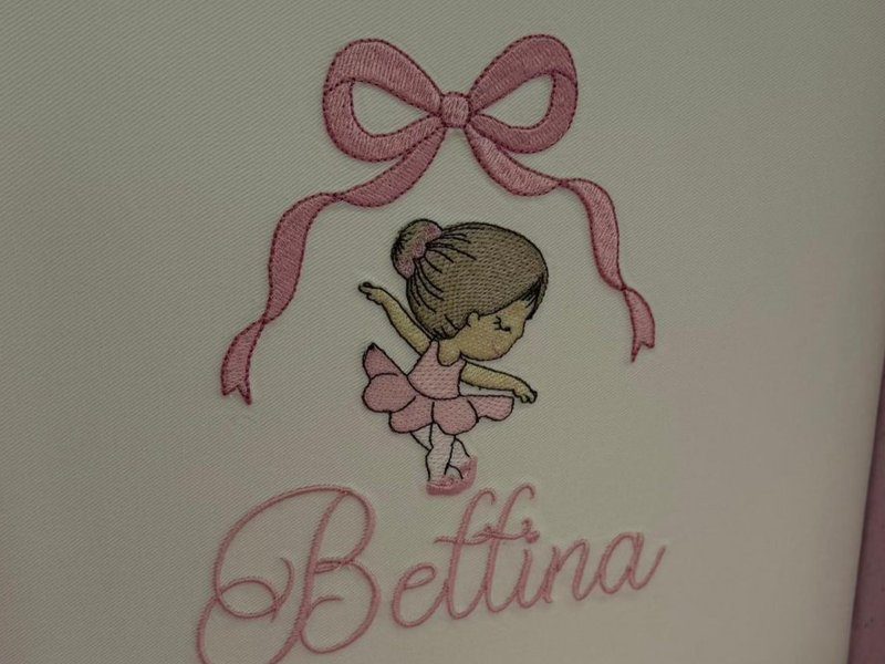La�o rosa de fitas longas, bailarina de coque e tutu, e Bettina em cursiva - o painel bordado inteiro da tampa