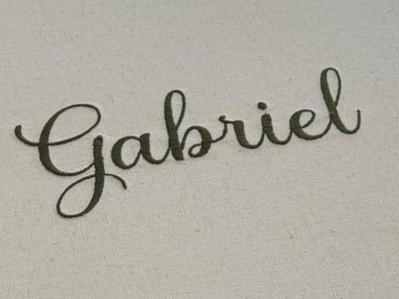 O nome Gabriel bordado em verde escuro na tampa externa de linho cru da caixa fechada