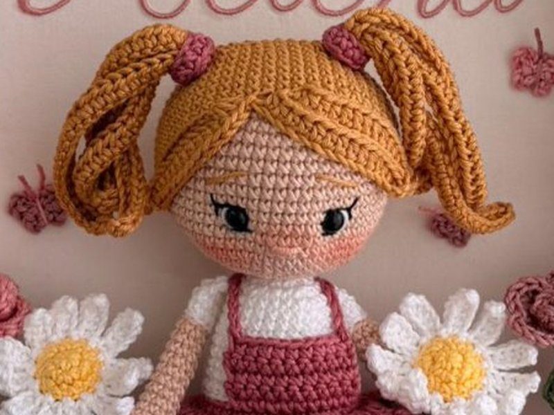 A boneca de croch� de cabelos loiros com maria-chiquinhas presas por el�stico e vestido salopete rosa