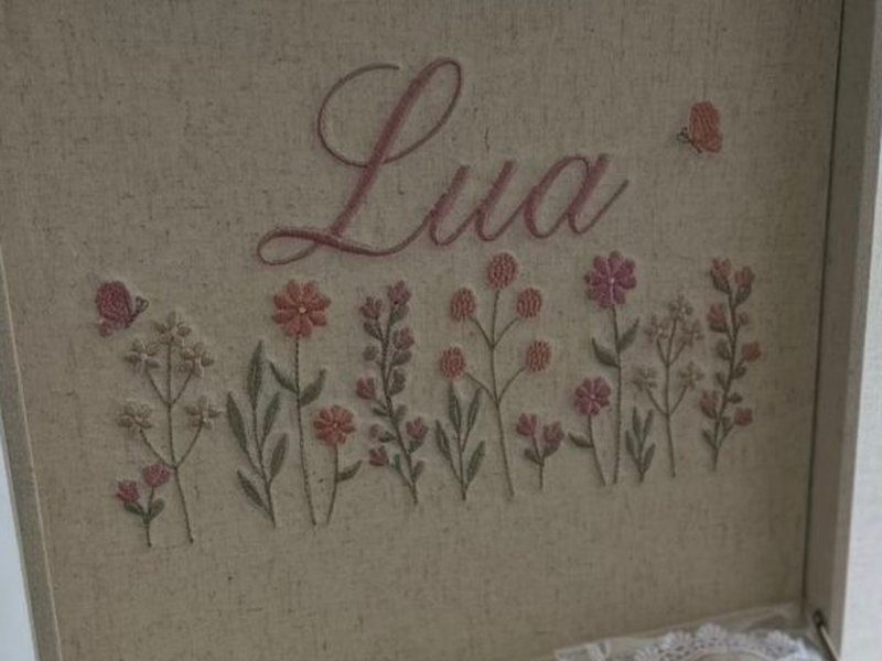 Lua bordado em cursiva ros� sobre uma faixa de flores do campo bordadas em ros�, coral e verde