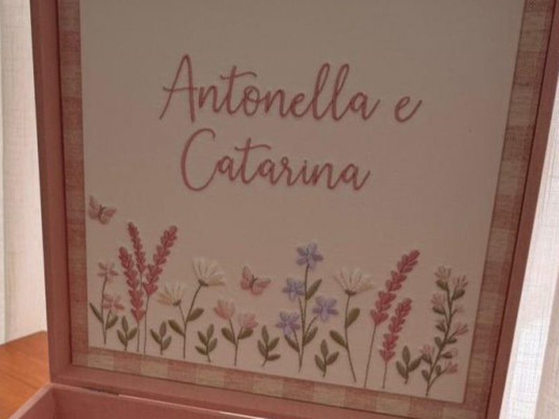 Antonella e Catarina bordados em duas linhas cursivas sobre flores rosa, lil�s e brancas com borboletas