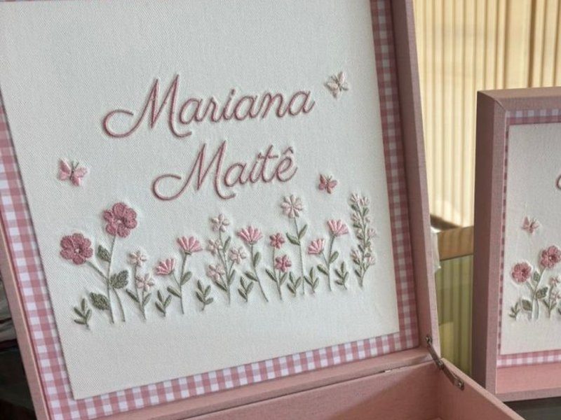 Mariana Mait� em duas linhas cursivas rosa sobre jardim de flores bordadas com borboletas, em moldura xadrez