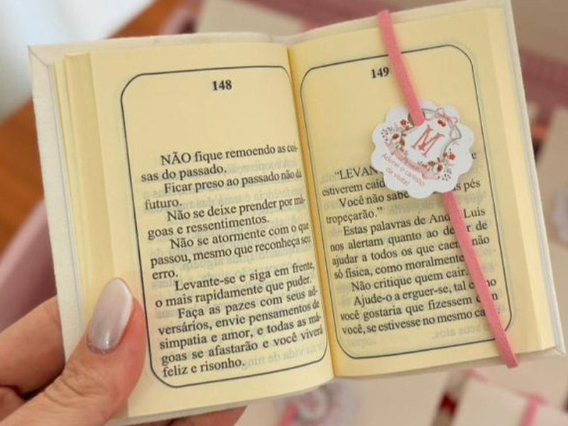 Livrinho aberto com p�ginas numeradas 148 e 149 e texto impresso, com o el�stico rosa e a tag
