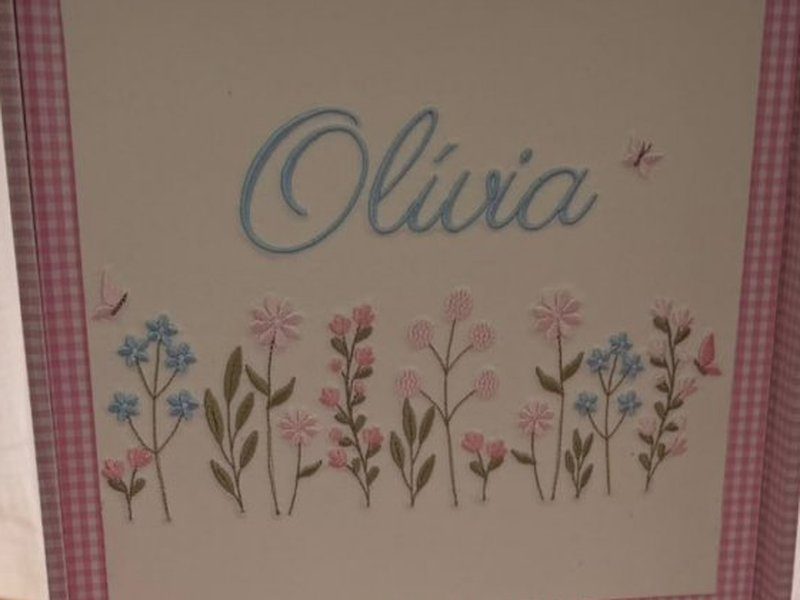 Ol�via bordado em azul-claro sobre flores rosa e azuis bordadas com borboletas