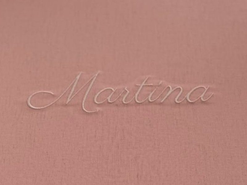 Martina bordado em cursiva branca, em relevo sobre a tampa rosa envelhecido