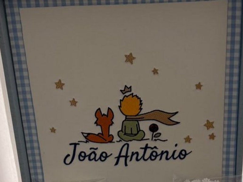 A raposa e o Pequeno Pr�ncipe bordados na tampa, com o nome Jo�o Ant�nio em cursiva marinho e estrelas de madeira aplicadas em volta