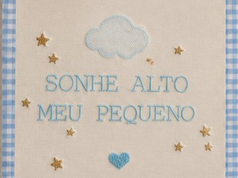 A frase SONHE ALTO MEU PEQUENO bordada em azul sob uma nuvem, entre estrelas douradas